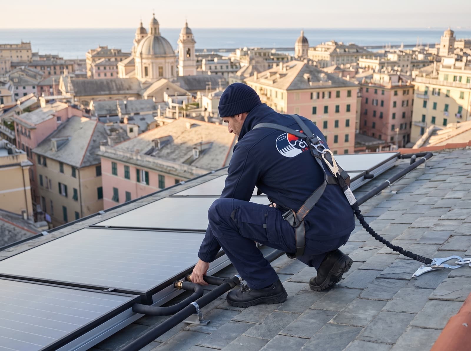 Tecnico Cigna Impianti, con imbracatura, controlla i pannelli solari termici su un tetto in ardesia di Genova
